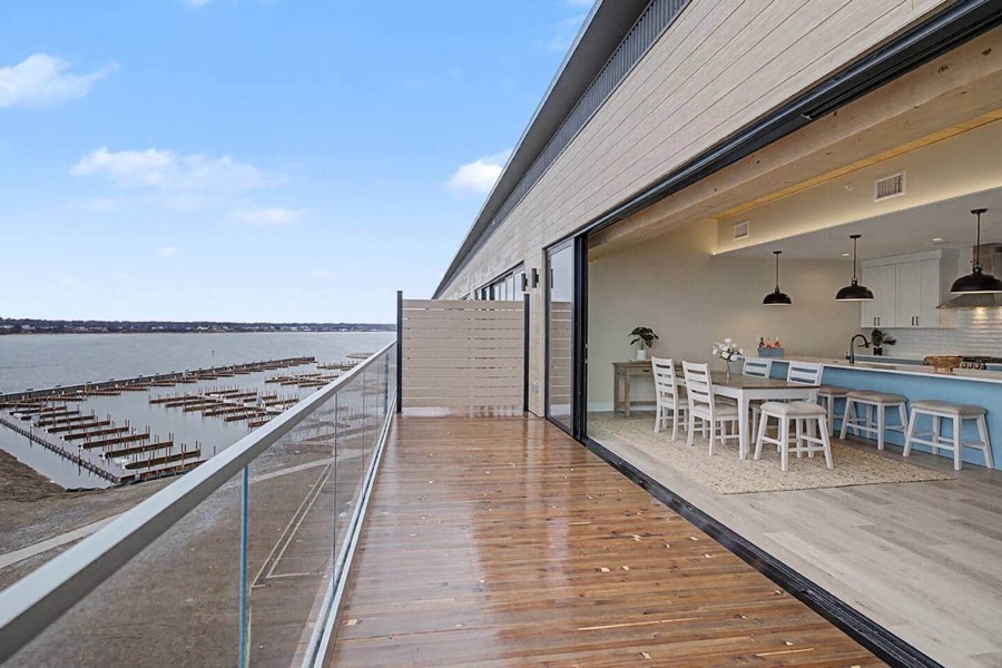 The private glass-railed deck looking straight down onto Adelaide Pointe's marina slips, with the glass wall open into the kitchen and dining space