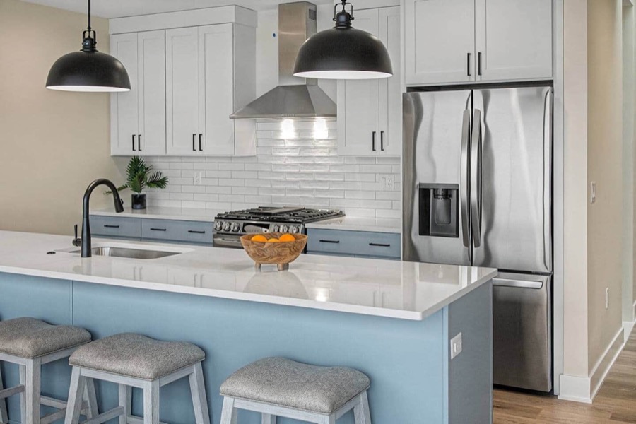 The kitchen's powder-blue island with three upholstered stools, white cabinetry, stainless fridge and hood, and black dome pendants