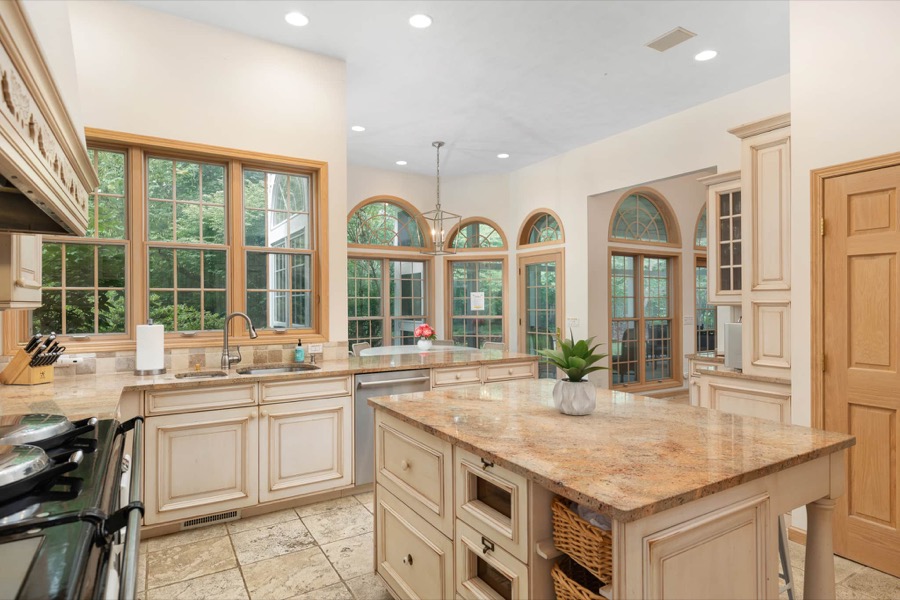 The chef's kitchen: cream cabinetry, granite counters, a broad center island, and a wall of windows under arched transoms