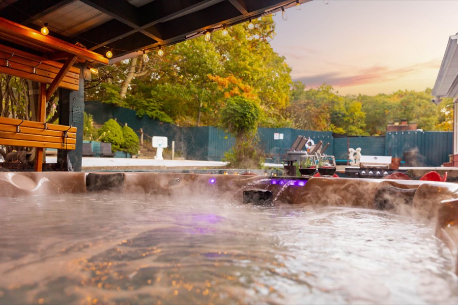 Steam rising off the hot tub at sunset, wine glasses on the rim, with the pool deck and basketball hoop beyond